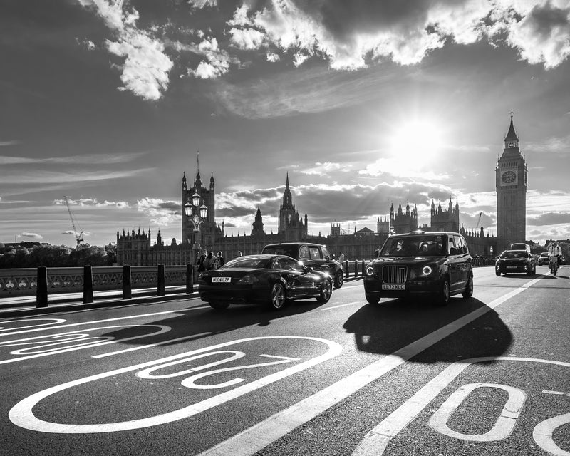 Black London taxi cab crossing Westminster Bridge with Big Ben and the Houses of Parliament silhouetted against a sunburst sky, black and white fine art photography print