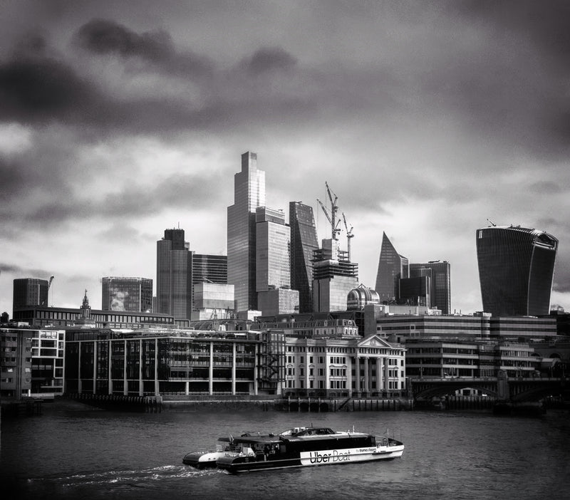 City of London skyline with Walkie Talkie, Cheesegrater and NatWest Tower under dramatic storm clouds, Uber Boat on the Thames in the foreground, black and white fine art photography print