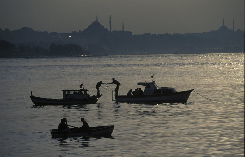 Silhouette of fishermen on three boats at dusk on the Bosphorus, with Süleymaniye Mosque and Istanbul skyline in the background, fine art photography print