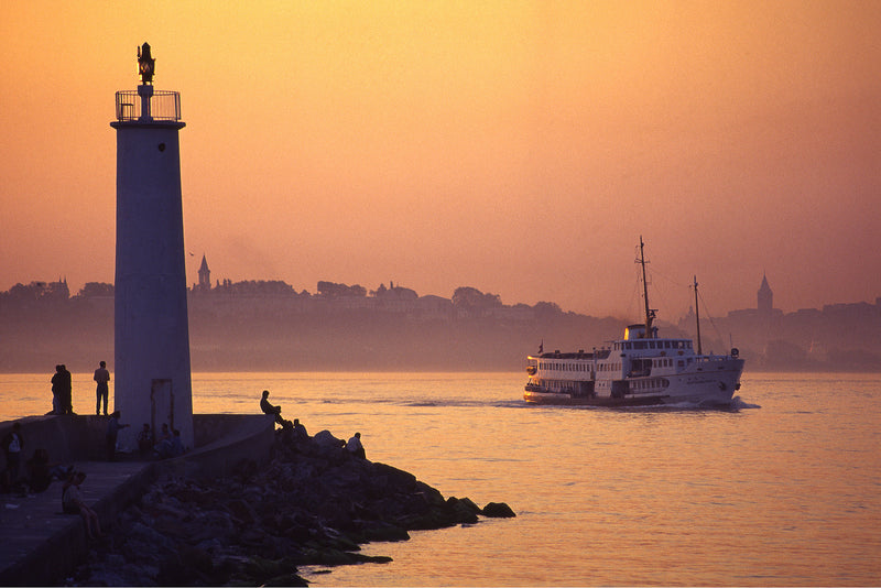 White lighthouse and Bosphorus ferry at amber sunset with Istanbul's historic skyline silhouetted in the mist, fine art photography print