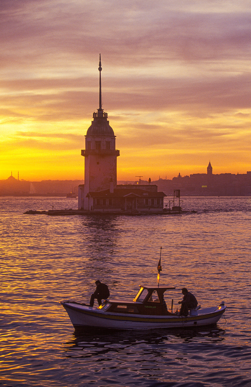 Maiden's Tower (Kız Kulesi) silhouetted against a vivid amber and violet sunset over the Bosphorus, with a fishing boat in the foreground, Istanbul fine art print