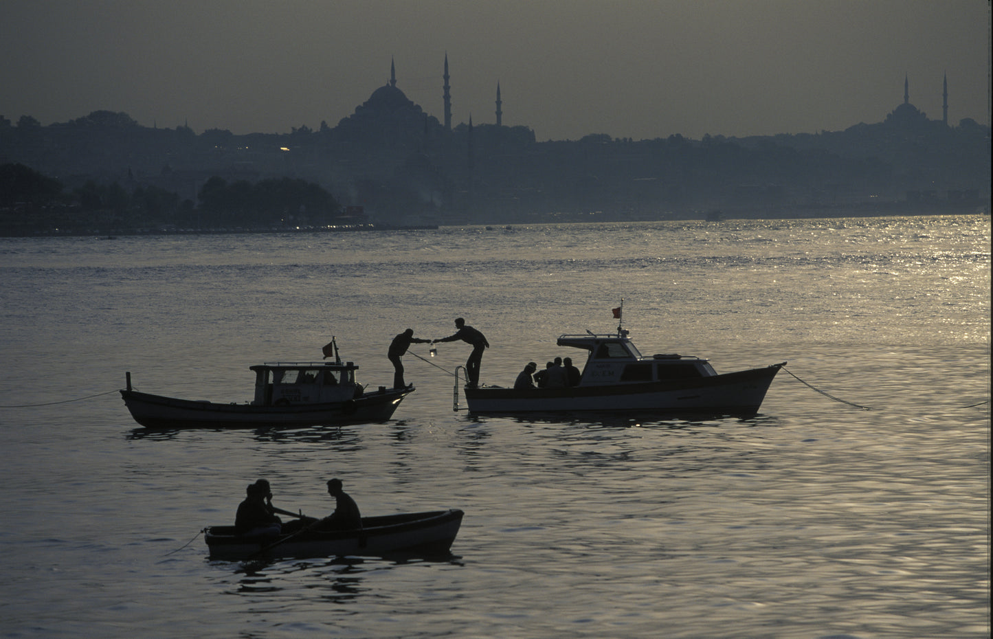 Silhouette of fishermen on three boats at dusk on the Bosphorus, with Süleymaniye Mosque and Istanbul skyline in the background, fine art photography print